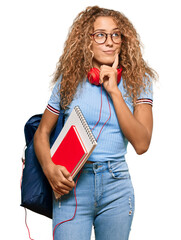 Beautiful caucasian teenager girl holding student backpack and books serious face thinking about...