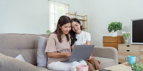 Mother and adult daughter sitting on the sofa together, mother and daughter using laptop to surf website together