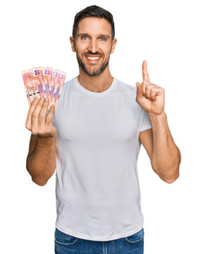 Handsome man with beard holding south african 50 rand banknotes surprised with an idea or question pointing finger with happy face, number one