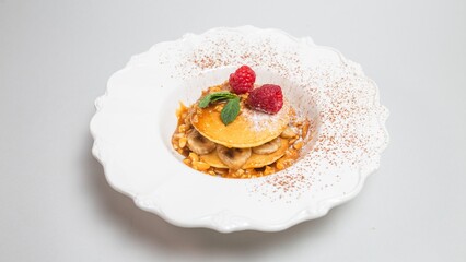 Delicious pancakes with banana-raspberry filling and maple syrup on a white background