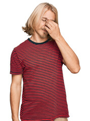 Caucasian man with blond long hair wearing casual striped t shirt tired rubbing nose and eyes feeling fatigue and headache. stress and frustration concept.