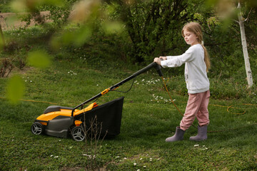 Little girl trimming lawn with mower, helping with houshold chores	