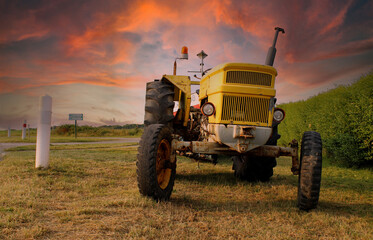 Old yellow tractor beside the road in the evening sun with colorful sunset