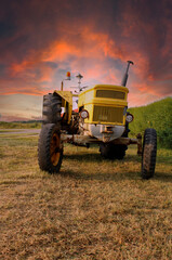 Old yellow tractor beside the road in the evening sun with colorful sunset