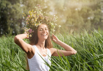 Delightful mood of a young woman. Beautiful happy young woman laughing outdoors with a wreath of flowers on her head.
