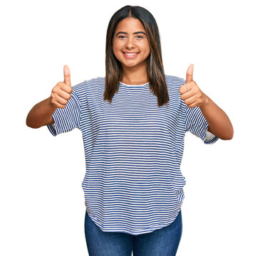 Young latin girl wearing casual clothes approving doing positive gesture with hand, thumbs up smiling and happy for success. winner gesture.