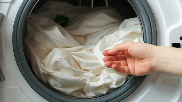 A person throws a laundry capsule into the drum of a washing machine.