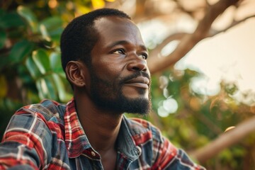 Portrait of a handsome african american man with a beard in a checkered shirt in the park. - obrazy, fototapety, plakaty