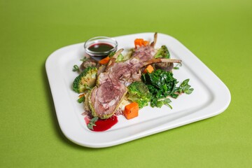 delicious ribs with vegetables and mushrooms on a white plate on a green background