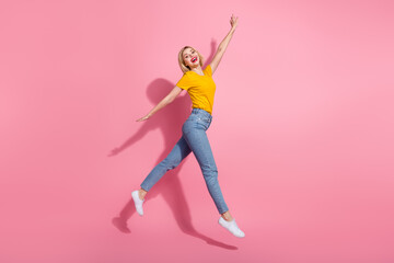 Full length photo of cute excited lady dressed yellow t-shirt jumping high having fun empty space isolated pink color background
