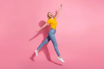  Full length photo of cute excited lady dressed yellow t-shirt jumping high having fun empty space isolated pink color background © deagreez