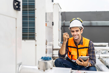 Happy male technical foreman inspects maintenance work holding a tablet and radio call with look at camera and smiling, He is control plumbing and electrical systems on the roof of a building