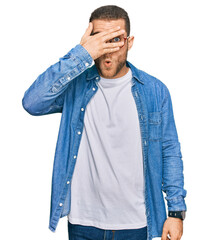 Young caucasian man wearing casual clothes peeking in shock covering face and eyes with hand, looking through fingers with embarrassed expression.