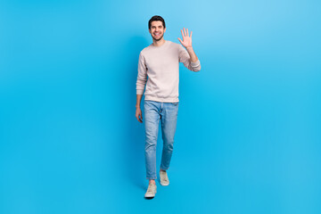 Full size photo of optimistic cheerful positive man wear sweatshirt denim pants waving palm say...
