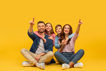 Happy family pointing up sitting together on yellow background