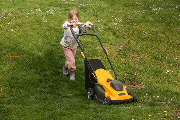 Little girl trimming lawn with mower, helping with houshold chores	