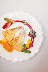 top view of an exquisite pancake with berries and cream on a white platter with red sauce