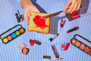 Promotional image of organic cosmetics products. Woman putting lipstick on toast bread against blue tablecloth. Concept of pop art photography, creativity, cosmetic, products, surrealism