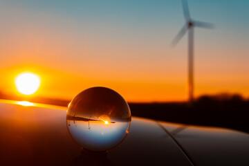 Crystal ball sunset with wind power plant silhouettes and reflections on a car roof near Kugl,...