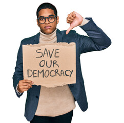 Young handsome hispanic man holding save our democracy protest banner with angry face, negative...