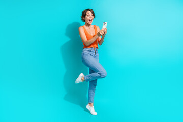 Full size photo of ecstatic nice girl dressed knitwear top denim pants astonished staring at smartphone isolated on blue color background - obrazy, fototapety, plakaty