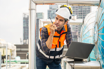 Male technical foreman inspects maintenance working in laptop and commands with talking on radio call with colleague with to look at plumbing and electrical systems on the roof of a building - obrazy, fototapety, plakaty
