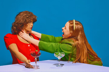 Young redhead woman sitting at table with mannequin and expressing stressful emotions against blue background. Concept of pop art photography, creativity, psychology, communication