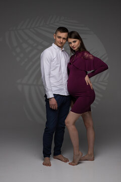 portrait of a pregnant couple on a grey background, pregnant couple posing in a studio, couple kissing, studio pregnancy photo shoot