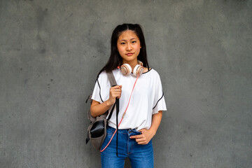 Teen Asian high school student girl standing outdoors looking at camera.