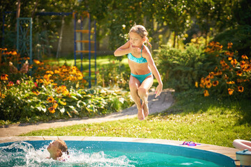 Cute little girl jumping into the swimming pool during summer