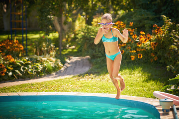 Little girl with goggles jumping into the swimming pool during summer