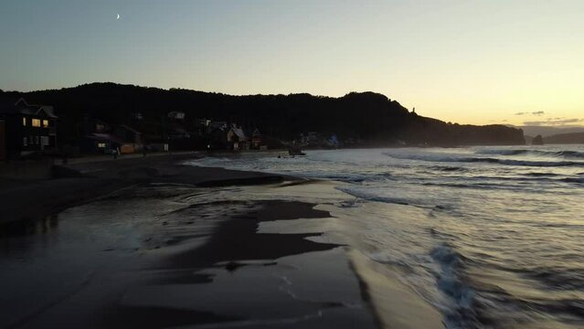 Drone footage of Shioya Beach with sea waves and cliff in the background at sunset in Otaru City