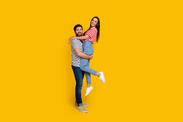 Fototapeta na wymiar Full size photo of nice couple dressed striped t-shirt cuddle together guy hold girlfriend on hands isolated on yellow color background
