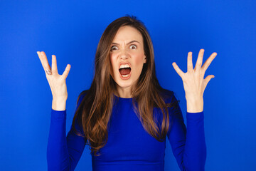 Screaming, hate, rage. Yelling emotional angry woman screaming on blue studio background....