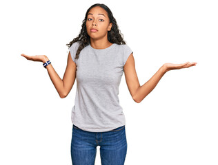 Young african american girl wearing casual clothes clueless and confused expression with arms and...
