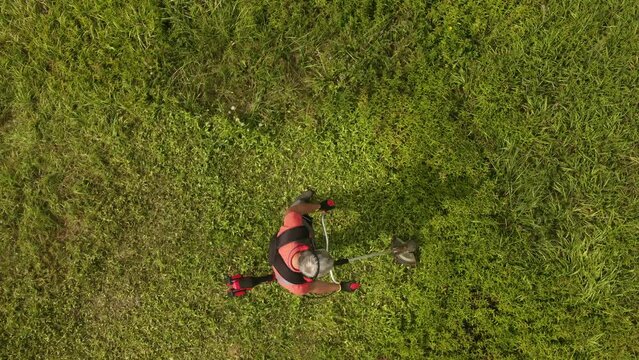 Aerial view of worker in protective clothing cutting grass with weed trimmer