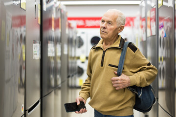 Senor man pensioner buying fridge in showroom of electrical appliance store