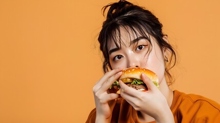 Generative AI : Young Asian woman eating hamburger on orange background - obrazy, fototapety, plakaty