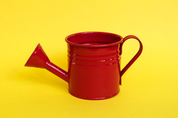 Red watering can on yellow background.  © gabriela