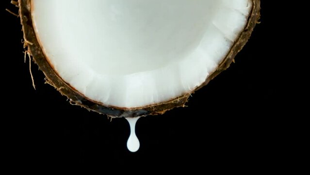 Coconut water juice dripping from half of a coconut on black background slow motion.