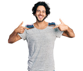 Young hispanic man wearing casual t shirt looking confident with smile on face, pointing oneself...