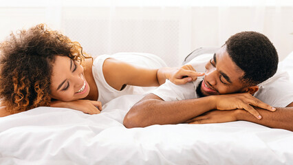 Cheerful woman touching her husband nose in bed