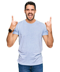 Fototapeta premium Young hispanic man wearing casual clothes shouting with crazy expression doing rock symbol with hands up. music star. heavy music concept.