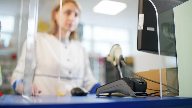 A close-up of a bank terminal to which a card is presented for payment. In the background you can see a woman pharmacist in a white coat who is kindly waiting. High quality 4k footage