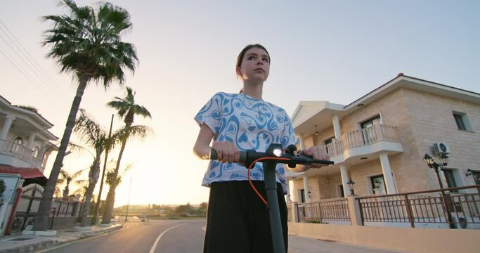A teenage girl rides an electric scooter on the street at sunset. Active lifestyle and sports of modern children. High quality 4k footage