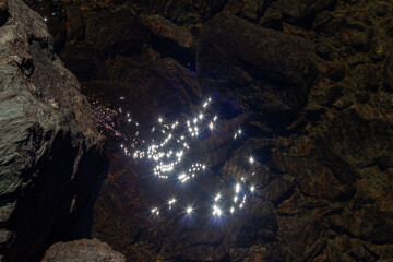 Twinkling lights in the dark water of a stream. A rock, crystal clear water.