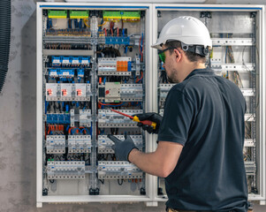 A male electrician works in a switchboard using an electrical connection cable.