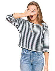 Fototapeta premium Beautiful blonde woman wearing casual clothes peeking in shock covering face and eyes with hand, looking through fingers with embarrassed expression.