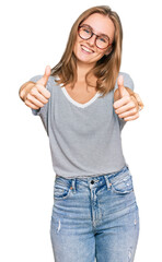 Beautiful young blonde woman wearing casual clothes and glasses approving doing positive gesture with hand, thumbs up smiling and happy for success. winner gesture.