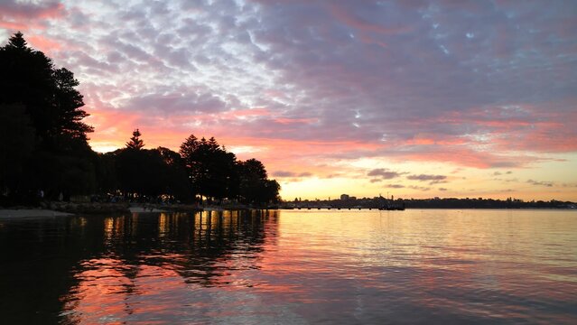 Spectacular sunset at Point Walter, Perth, Western Australia.  The swimming beach and the fishing jetty is visible in the distance. Beautiful sunset colors are reflected off the Swan River water.